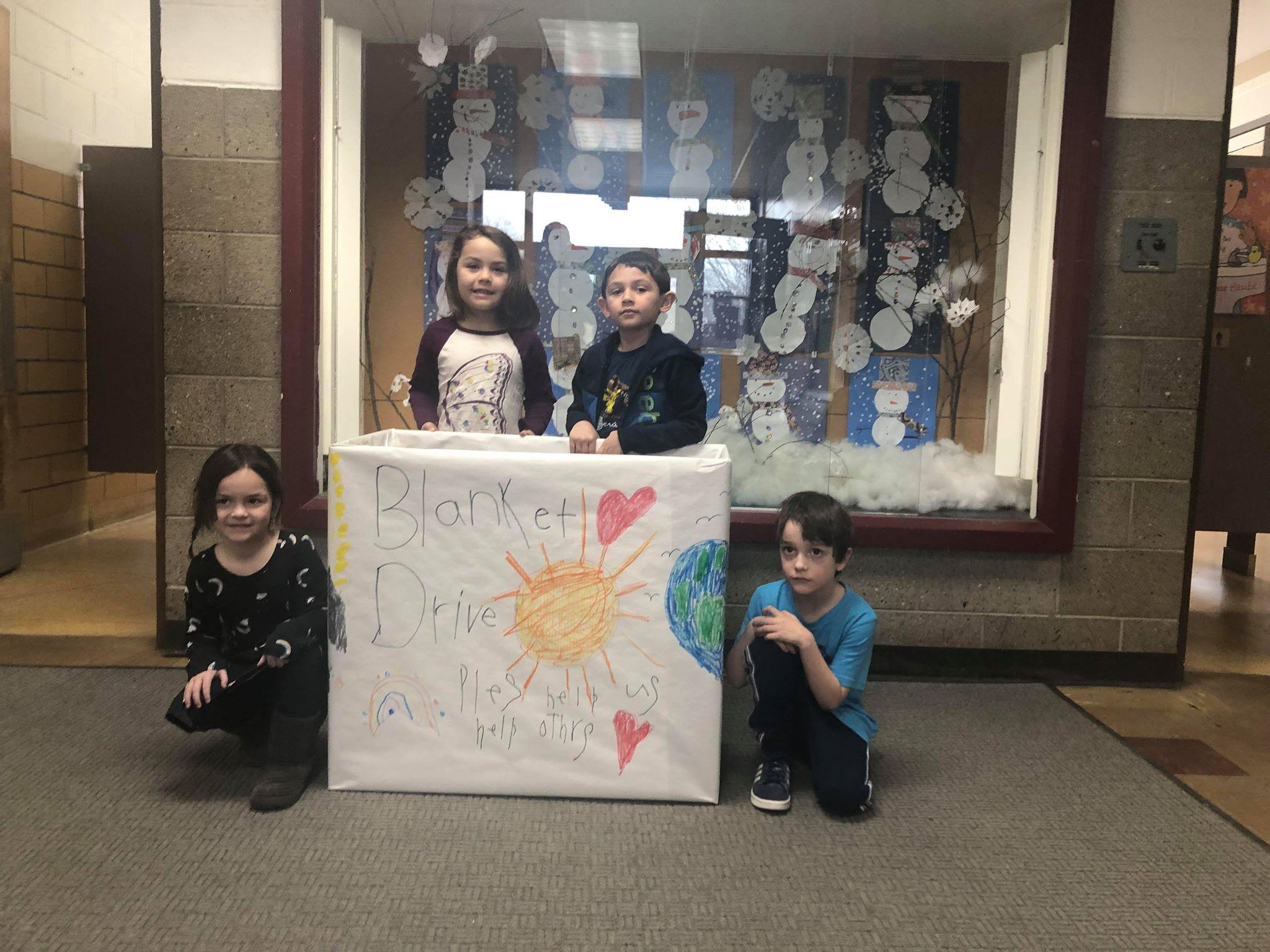 four kindergarten students posing with a collection box that says "Blanket drive - Please help us help others"